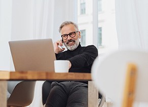 Man with glasses smiling while working on laptop