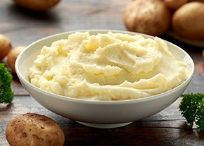 Bowl of mashed potatoes surrounded by whole potatoes