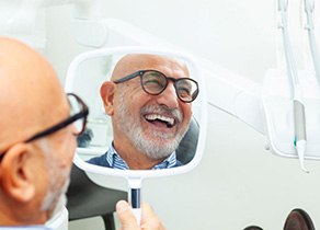 Face of happy senior dental patient reflected in hand mirror