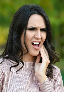 Woman in sweater rubbing jaw in pain