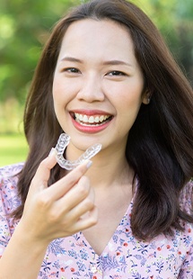 Woman standing outside smiling and holding clear aligner