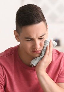 Man in red shirt holding towel over jaw