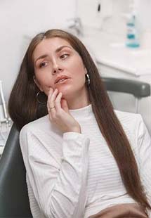 Woman in dental chair rubbing jaw in pain