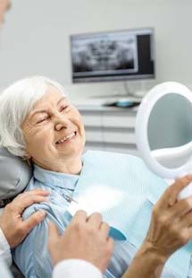 Senior woman sitting in dental chair and looking at smile in handheld mirror