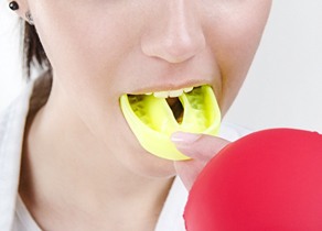 Close up view of a person preparing to insert a yellow mouthguard into their mouth