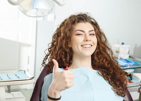 Woman sitting in dental chair giving a thumbs up