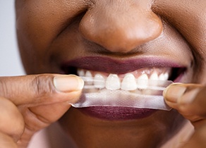 Patient placing whitening strip on top teeth