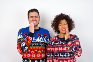 couple wearing holiday sweaters holding their faces in dental pain