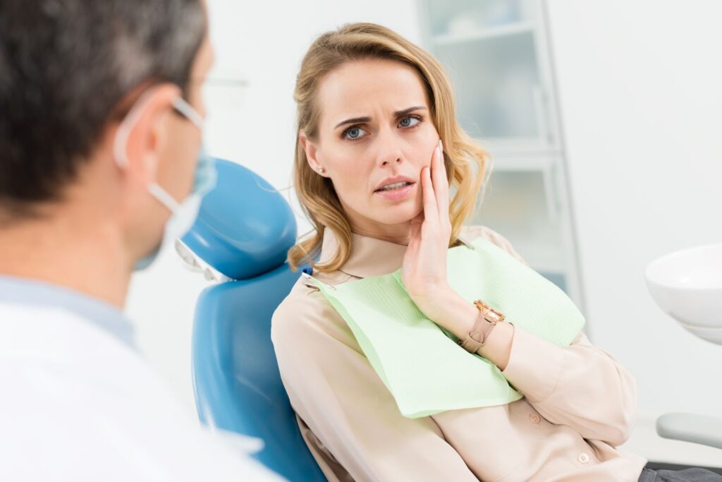 A woman in a dental chair holding her jaw in pain